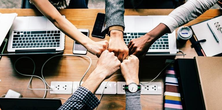 A diverse group of people in a circle fist bump on another in collaboration