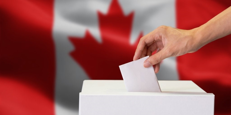 A hand dropping a ballot into a box; the Canadian flag in the background.