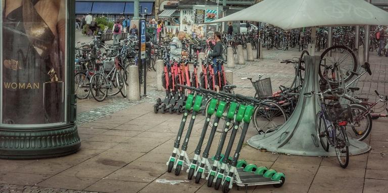 Un trottoir de la ville avec une rangée de scooters électriques alignés dessus.