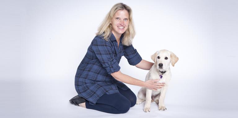 A volunteer puppy raiser sits beside a Golden Retriver puppy at a professional photoshoot. 