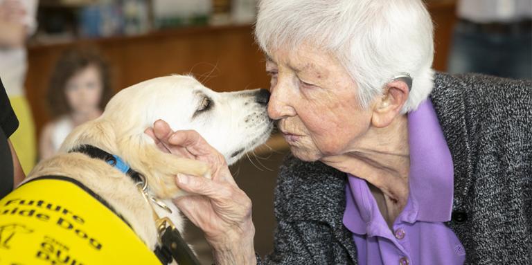 A woman getting a kiss from a yellow Golden Retriever puppy.