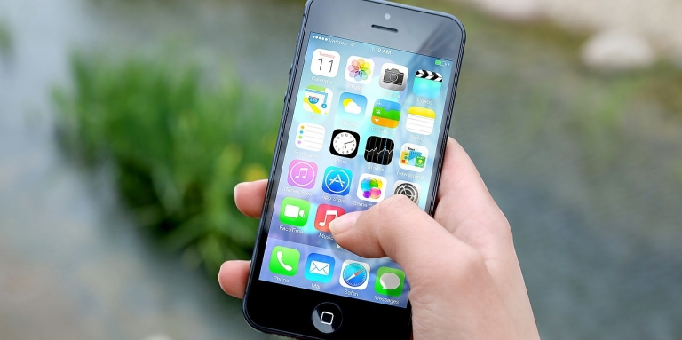 une main tenant un iPhone, on voit plusieurs icônes d'applications.