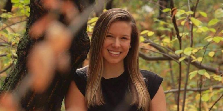 Kimberly Blain, leaning against a tree in a forest during the Autumn season. 