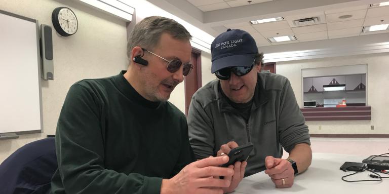 Lloyd Buckler, assis à une table, aidant quelqu'un à apprendre à utiliser son iPhone. 