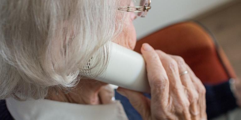 An elderly woman holds a landline telephone to her ear. 