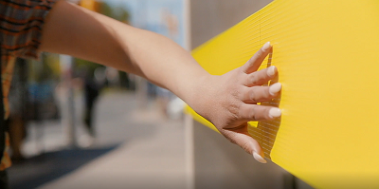 Une image d'une main tendant la main pour toucher un signe braille en jaune INCA