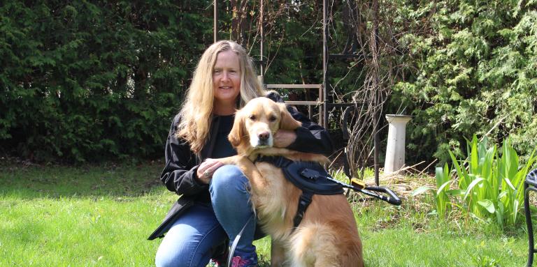 Diane Bergeron à genoux dans l'herbe à côté de son chien-guide Carla, un golden retriever.