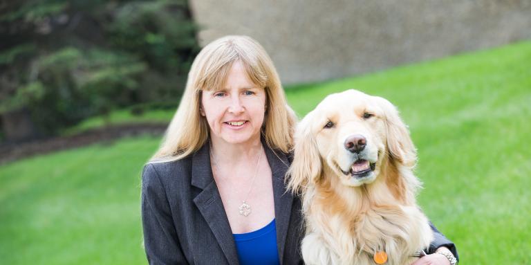 A woman kneels down beside her golden retriever guide dog. 