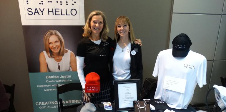 Denise Justin and friend sit at her "Say Hello to Blindness" exhibitor display table.