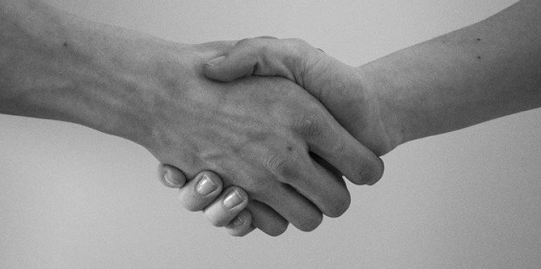 A black & white photograph of two hands extended and shaking. 