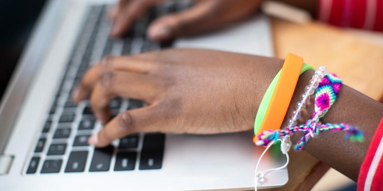 The hands of a teenager wearing friendship bracelets typing on a laptop computer.