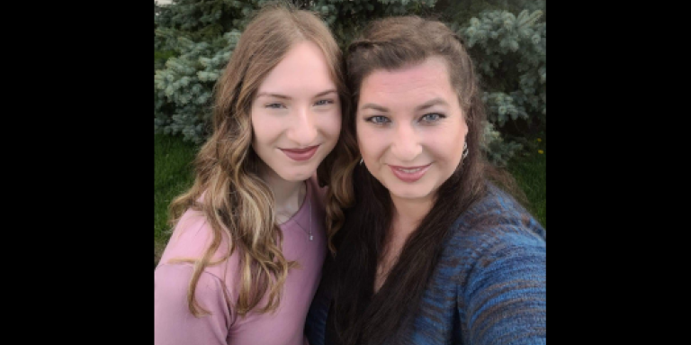 Emma (left) and Michelle (right) smile and pose for a photo in front of a beautiful green tree.