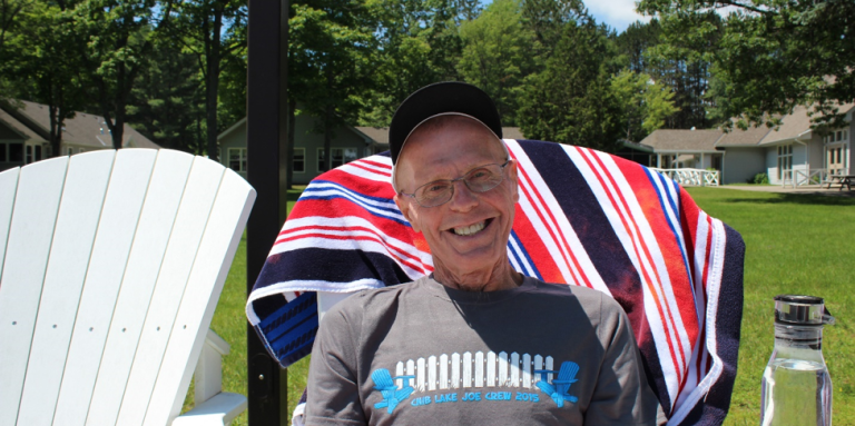 Jim (and his megawatt smile) sits in a Muskoka chair near the shores of CNIB Lake Joe.  