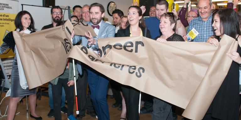 David accompagné d'employé et de personnes aveugles défonce une barrière de papier symbolique.