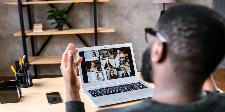 Une photo au dessus de l'épaule d'un homme qui participe à une conférence en ligne sur son ordinateur portable.