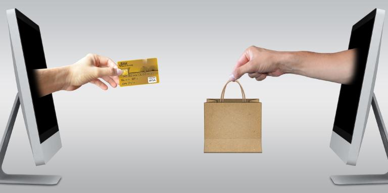 Deux ordinateurs de bureau avec des images photoshoppées de mains sortant des moniteurs. Sur l'écran de l'ordinateur de gauche, une main est tendue et tient une carte de crédit. Sur l'ordinateur de droite, une main tendue tient un sac à provisions.