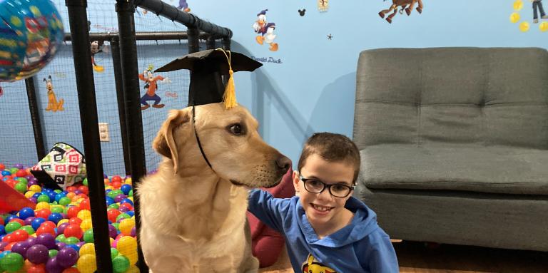 Un jeune portant des lunettes à genoux à côté de son chien compagnon portant un mortier.