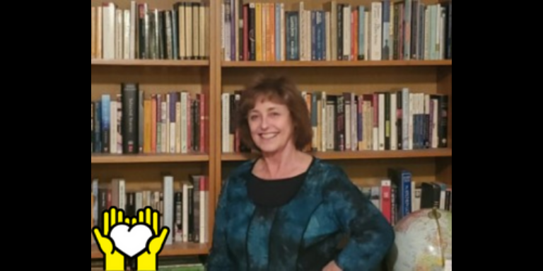 Une photo de Lynn Kennedy posant en face d'une étagère de livres.  L'icône de deux mains tenant un cœur blanc sur un fond jaune, dans le coin inférieur gauche.