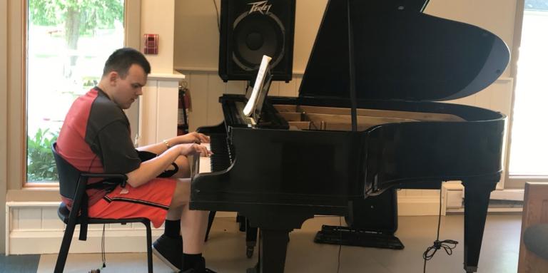 Daniel Kisielewski, guest at CNIB Lake Joe Adult Week 2022, playing the black grand piano in the CNIB Lake Joe lounge.