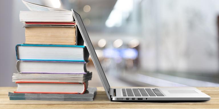 Une pile de livres à côté d'un ordinateur portable posés sur une table en bois.