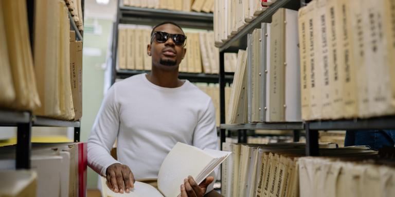 Image d'un jeune adulte qui lit un manuel braille assis dans une rangée de bibliothèque