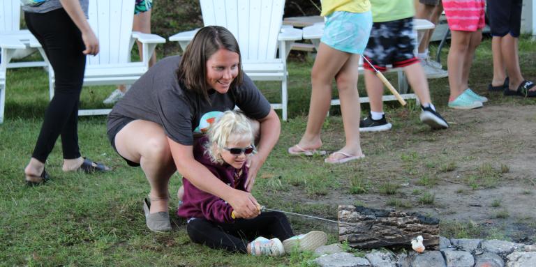 A mother and daughter roast a marshmallow over a campfire at CNIB Lake Joe. 
