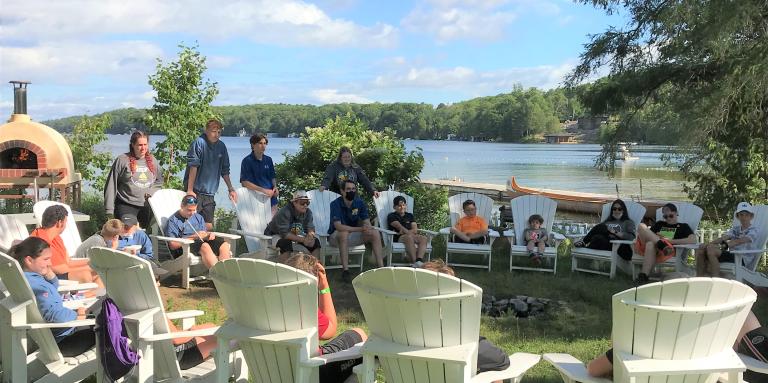 A group of children sit in Muskoka chairs around the outdoor pizza oven at Lake Joe.