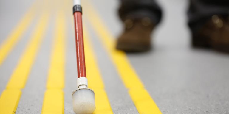 A white cane being used on pavement with raised yellow lines.