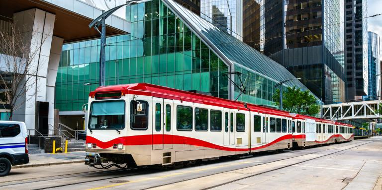 A red and white CTrain car glides along an outdoor light rail track in downtown Calgary. 