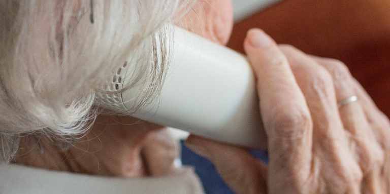 Une femme aînée porte un téléphone avec fil à son oreille.