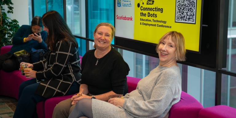 Deux femmes sont assises sur un canapé avec un panneau Connecting the Dots derrière elles.