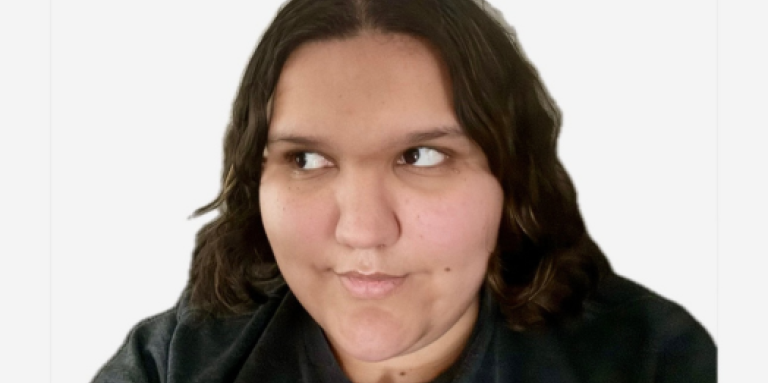 Kaitlynn, une jeune femme aux cheveux bruns, sourit et pose pour une photo de type selfie. Kaitlynn a les cheveux bruns et porte un t-shirt gris. 