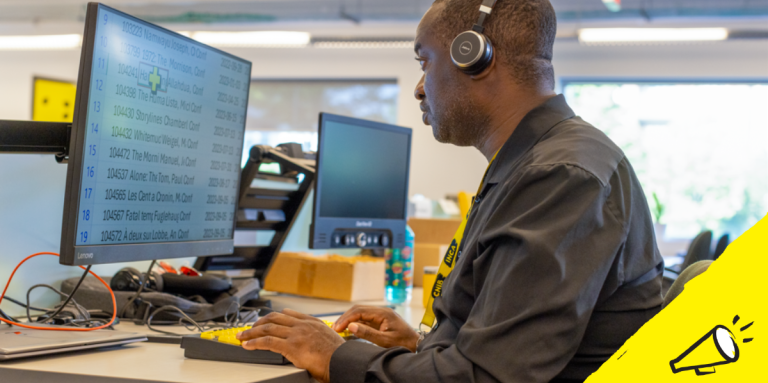 un homme est assis à un bureau et utilise une technologie d'agrandissement d'écran sur un ordinateur de bureau, ainsi qu'un clavier à contraste élevé.] 