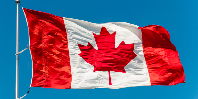 Un drapeau canadien flotte au sommet d'un mât, sur fond de ciel d'un bleu éclatant.