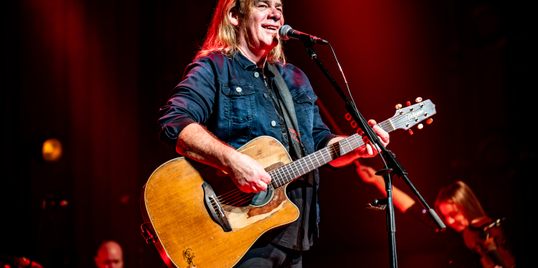 Le musicien Alan Doyle se tient sur scène devant un micro, une guitare à la main
