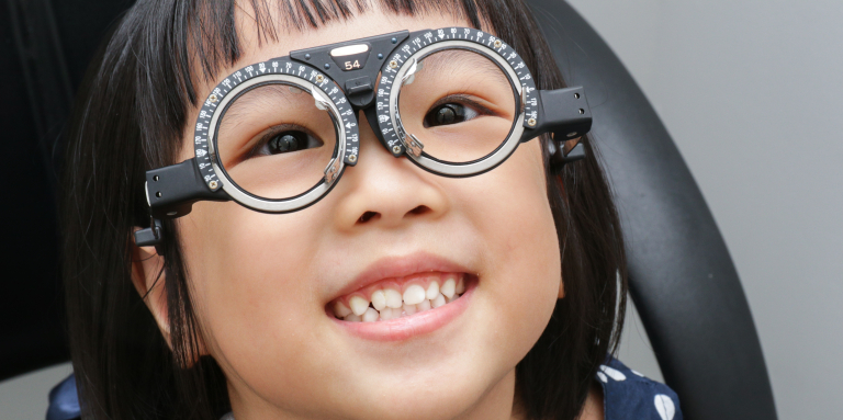Une jeune fille souriante porte une monture d'essai avec des verres réglables lors d'un examen de la vue.