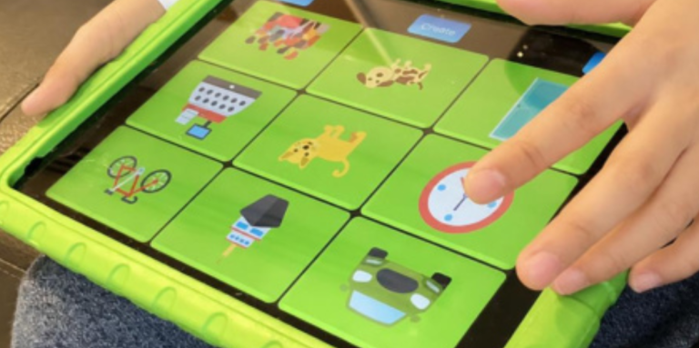 Les mains d’un enfant tiennent un iPad dans un étui de protection vert vif et tapotent une grille d’icônes colorées représentant notamment des animaux, des objets et une horloge à l’écran.