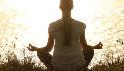 A woman sits in a cross legged yoga position with her hands in front of her in prayer.