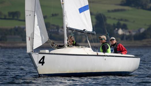 Joshua Cook et deux autres personnes sont assises dans un bateau à voile sur l'eau. Ils sont aux championnats du monde de voile aveugle en Ecosse.