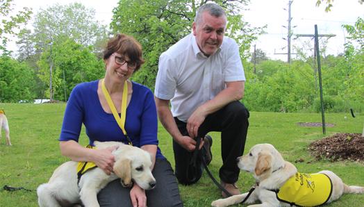 Karen et Andrew en compagnie de deux chiots vêtus d'un gilet jaune.