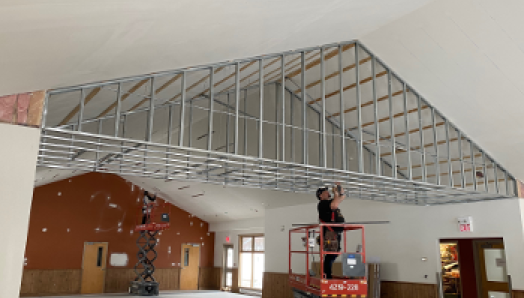 The Dining Hall & Lounge at CNIB Lake Joe. A construction worker stands on a large lift to reach the ceiling with a tool. 