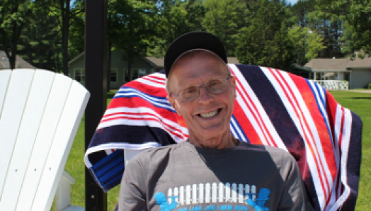 Jim (and his megawatt smile) sits in a Muskoka chair near the shores of CNIB Lake Joe.  