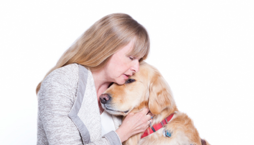 Diane Bergeron s’accroupit pour une photo aux côtés de Lucy sa chienne-guide. Lucy pose sa tête sur l’épaule de Diane qui la flatte avec amour.