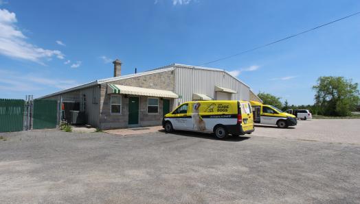 Exterior of Canine Campus in Carlton Place. Three CNIB Guide Dogs vans parked out front, trees and blue skies in the background.