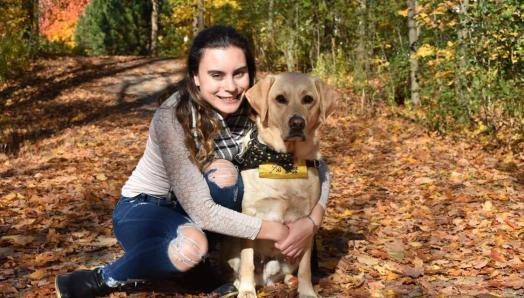 Danika and Ulysses sitting on the ground in a forest in Autumn. Danika has her arms wrapped around Ulysses for a huge hug.