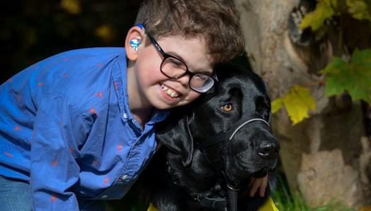 Kaiden, 10 ans, souriant et penché pour embrasser son chien compagnon d’INCA, Flinn, un croisement labrador retriever.