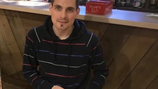 Ryan Hooey sitting in a restaurant, holding an insulin pump and smiling for the camera.