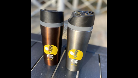 Tasses de voyage en acier inoxydable de couleur bronze et charbon de bois, avec couvercle noir sur une table au camp.