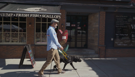 Lawrence et son chien-guide Lewis marchant sur le trottoir lors d’une journée ensoleillée.