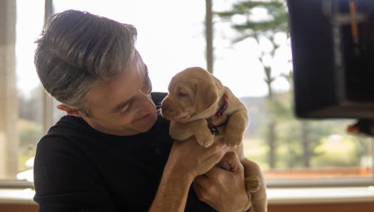 Ben Mulroney tenant un chiot d'à peine quelques semaines, un Labrador-Retriever jaune.